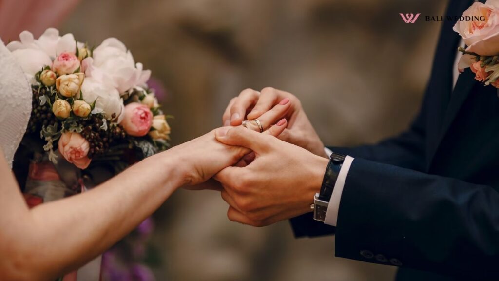 Groom placing a ring on the bride’s finger with a bouquet in hand.