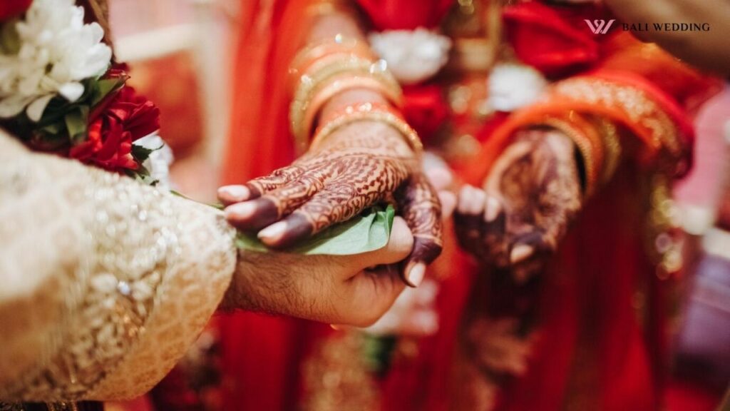 The bride's henna-covered hands placed on a green leaf, held by the groom, symbolizing a sacred moment of bonding during the wedding ceremony.