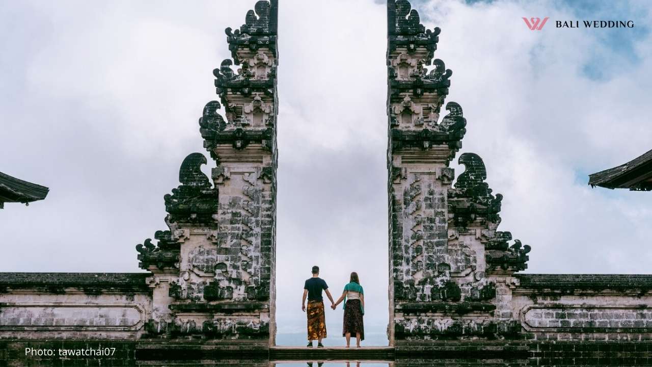 A couple holds hands while standing at the famous Gates of Heaven at Lempuyang Temple in Bali, with an expansive view of the horizon behind them, symbolizing a spiritual and majestic setting for a wedding.