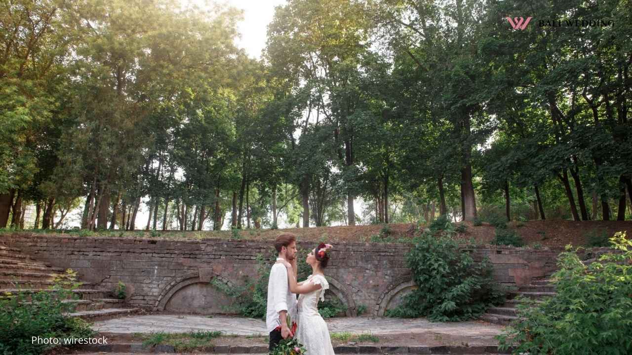 Bride and groom standing in an outdoor amphitheater surrounded by trees, sharing an intimate moment.