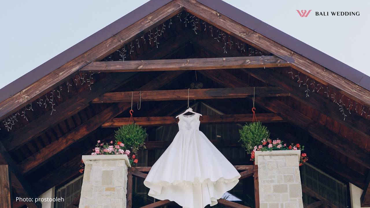 Wedding dress hanging elegantly on a rustic wooden beam at a wedding venue.