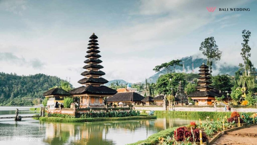 A stunning view of Ulun Danu Temple situated on the edge of a tranquil lake, with mountain ranges in the background and clear skies. This iconic Bali location is a perfect spot for a serene wedding ceremony.