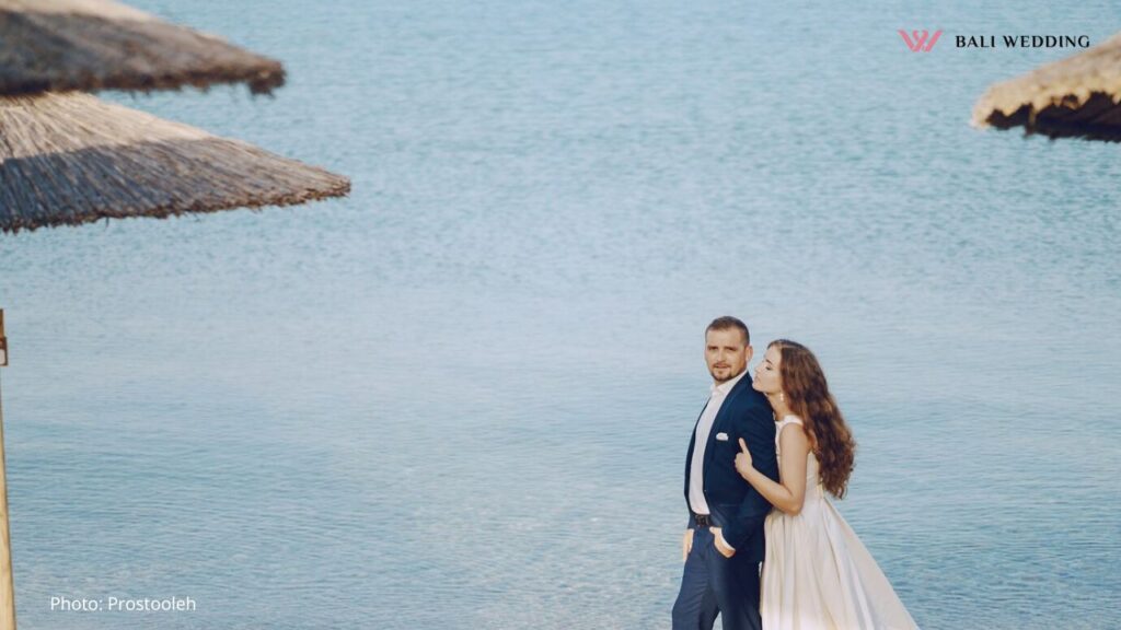 Beautiful young long-haired bride in white dress with her young husband on the beach