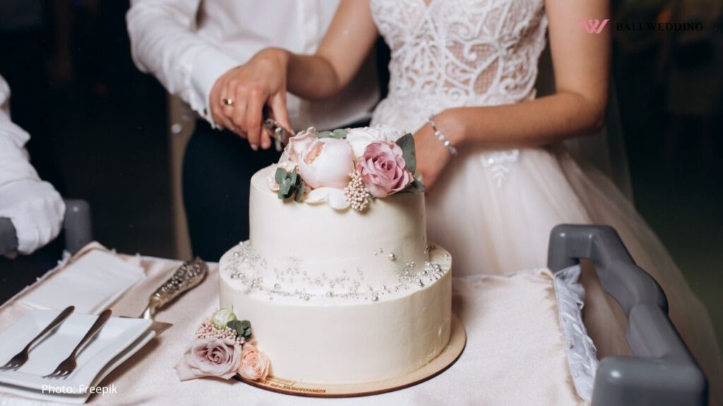 Bride and groom are cutting decorated with flowers wedding cake