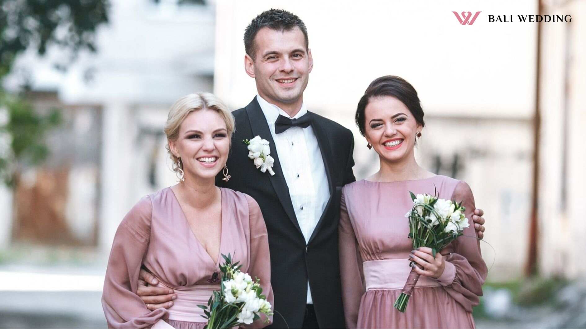 Groomsman embracing two bridesmaids standing outside